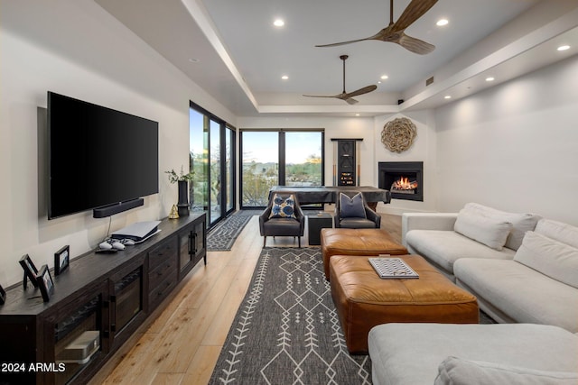 living room featuring a raised ceiling, ceiling fan, and light hardwood / wood-style floors