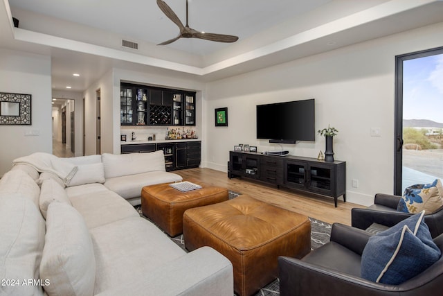 living room featuring light hardwood / wood-style floors, a raised ceiling, and indoor bar