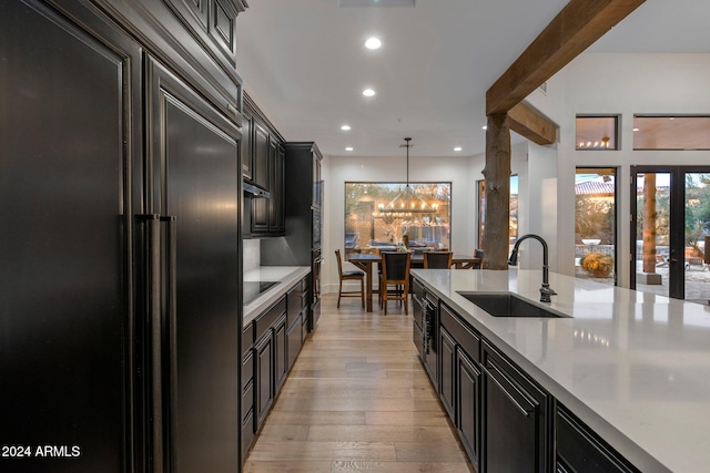 kitchen featuring paneled refrigerator, sink, beamed ceiling, light hardwood / wood-style floors, and hanging light fixtures