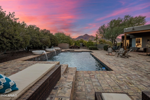 pool at dusk with a mountain view, a patio, pool water feature, and a fire pit