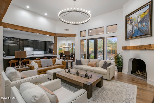 living room featuring french doors, a towering ceiling, a chandelier, and light wood-type flooring