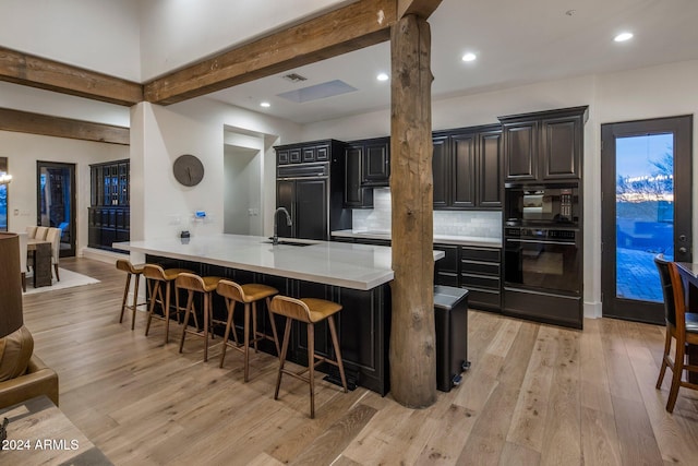 kitchen featuring backsplash, sink, light wood-type flooring, paneled fridge, and a kitchen bar