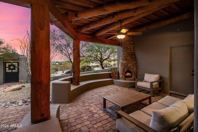 patio terrace at dusk with an outdoor living space with a fireplace and ceiling fan