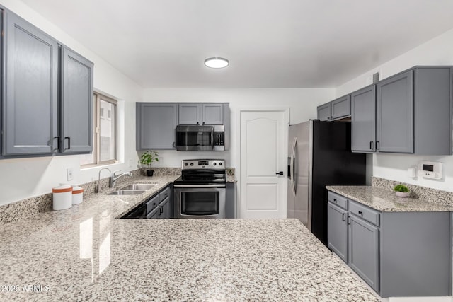 kitchen with stainless steel appliances, sink, light stone counters, and gray cabinets