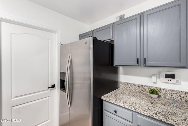 kitchen with light stone counters, stainless steel fridge, and gray cabinetry