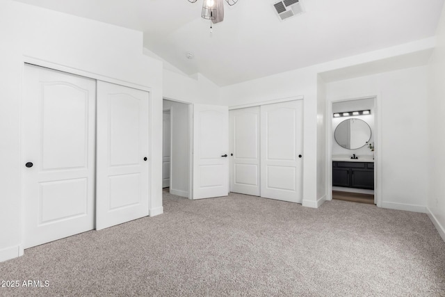 unfurnished bedroom with vaulted ceiling, two closets, light colored carpet, and ensuite bath