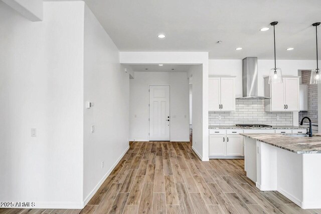 kitchen with pendant lighting, wall chimney range hood, sink, light stone counters, and white cabinets