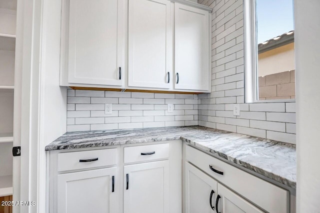 kitchen featuring light stone countertops, decorative backsplash, and white cabinets