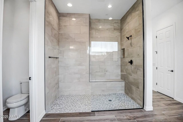 bathroom with toilet, hardwood / wood-style floors, and a tile shower