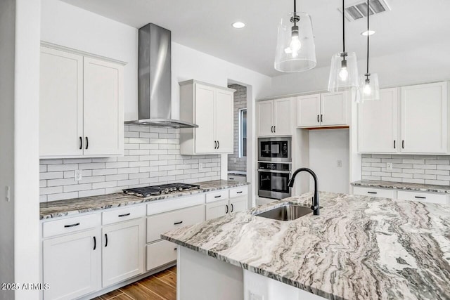 kitchen with appliances with stainless steel finishes, pendant lighting, sink, white cabinets, and wall chimney exhaust hood