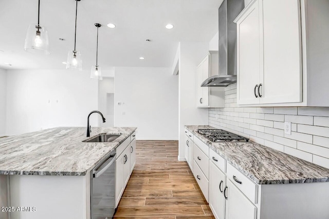 kitchen featuring hanging light fixtures, wall chimney range hood, a center island with sink, and white cabinetry