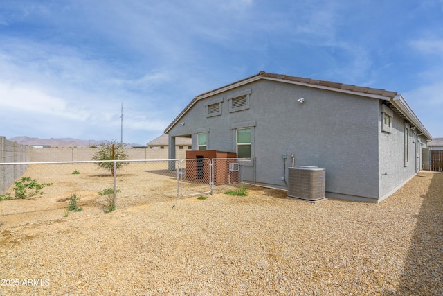 rear view of house featuring central AC, fence, a gate, and stucco siding