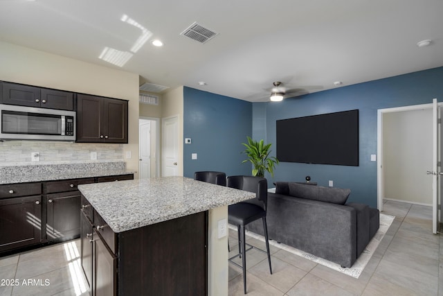 kitchen featuring a kitchen island, visible vents, decorative backsplash, stainless steel microwave, and a kitchen bar