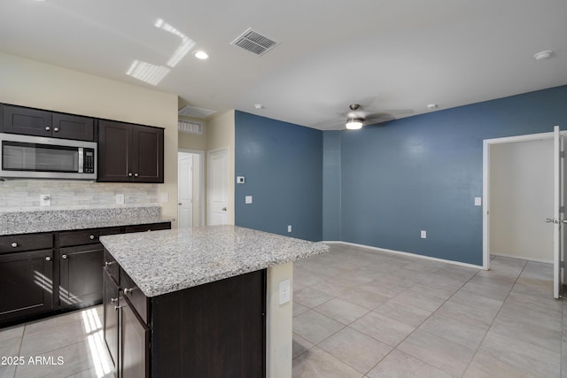 kitchen featuring light tile patterned floors, ceiling fan, visible vents, tasteful backsplash, and stainless steel microwave