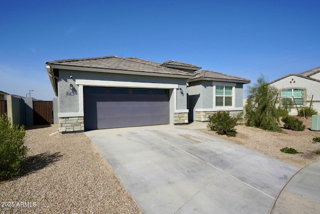 prairie-style home featuring an attached garage, fence, stone siding, concrete driveway, and stucco siding