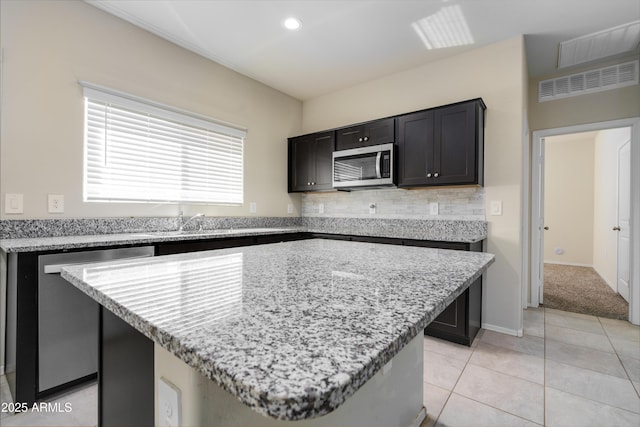 kitchen with light tile patterned floors, light stone counters, a kitchen island, appliances with stainless steel finishes, and backsplash