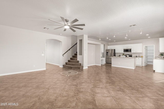 unfurnished living room featuring arched walkways, stairs, visible vents, and baseboards