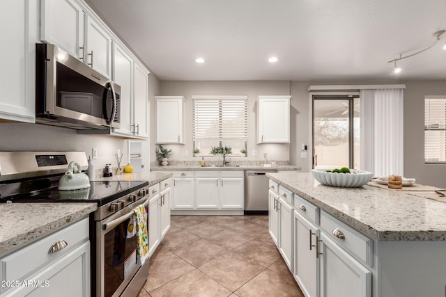 kitchen with appliances with stainless steel finishes, a healthy amount of sunlight, light stone countertops, and white cabinets