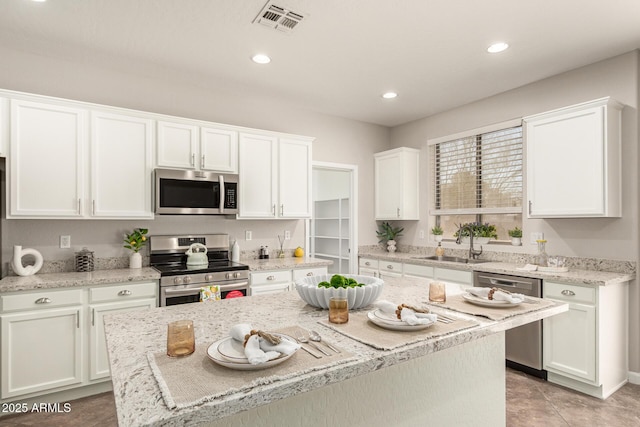 kitchen featuring stainless steel appliances, a sink, white cabinetry, and a center island