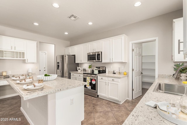 kitchen featuring stainless steel appliances, white cabinetry, a sink, and light stone counters