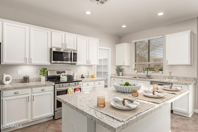 kitchen featuring white cabinets, stainless steel appliances, a sink, and a center island