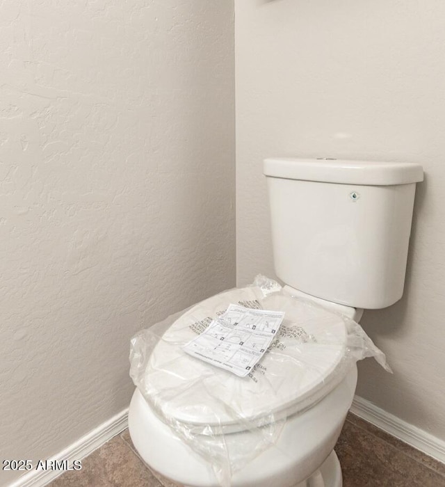 bathroom featuring toilet, baseboards, and a textured wall