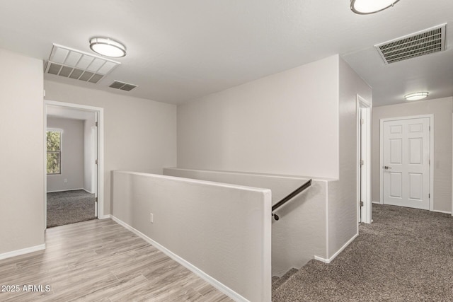 hallway with baseboards, visible vents, light wood finished floors, and an upstairs landing