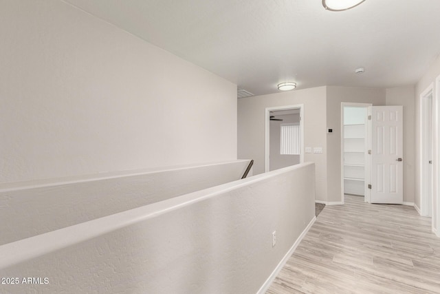 hallway featuring light wood finished floors, an upstairs landing, and baseboards