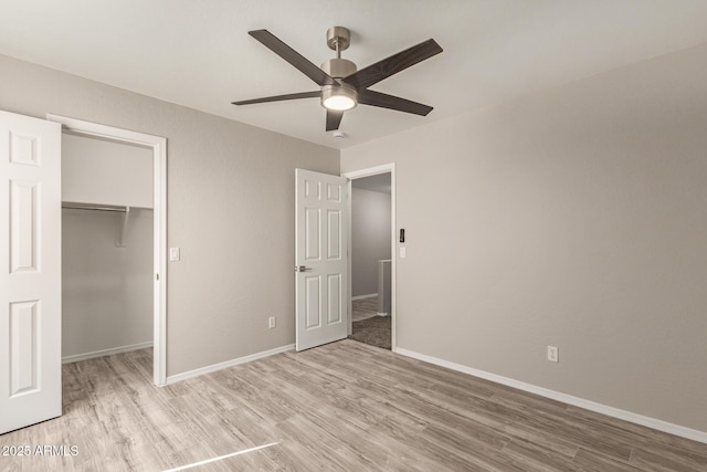 unfurnished bedroom featuring baseboards, a ceiling fan, light wood-style flooring, a spacious closet, and a closet