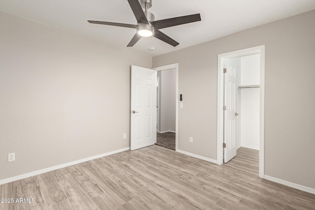 unfurnished bedroom featuring a closet, a spacious closet, a ceiling fan, light wood-type flooring, and baseboards