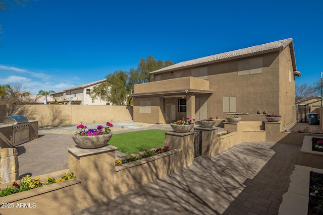 back of house featuring a patio, stucco siding, exterior kitchen, a fenced backyard, and a tiled roof