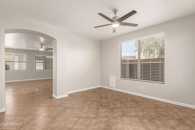 spare room featuring a ceiling fan, arched walkways, and baseboards