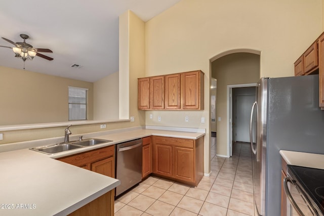 kitchen with arched walkways, light tile patterned flooring, a sink, light countertops, and appliances with stainless steel finishes