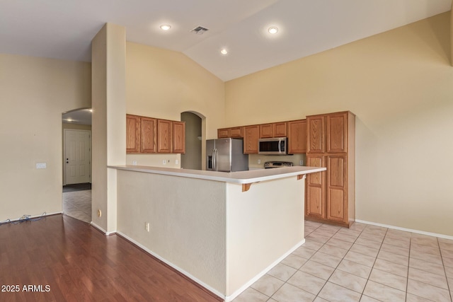 kitchen with arched walkways, stainless steel appliances, light countertops, visible vents, and a peninsula