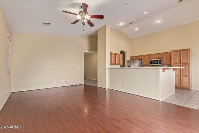 unfurnished living room with arched walkways, light wood finished floors, visible vents, and a ceiling fan