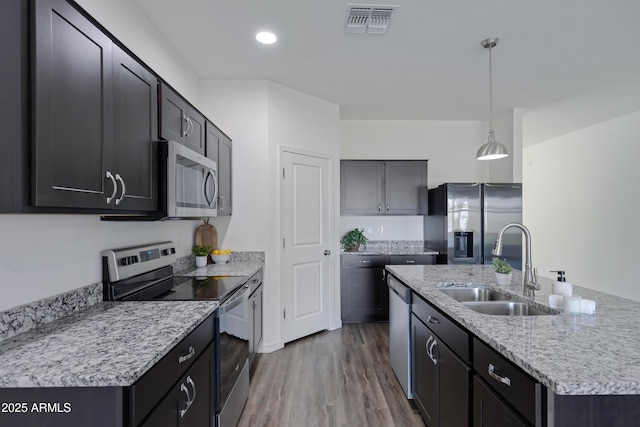 kitchen with appliances with stainless steel finishes, hardwood / wood-style floors, sink, hanging light fixtures, and a kitchen island with sink