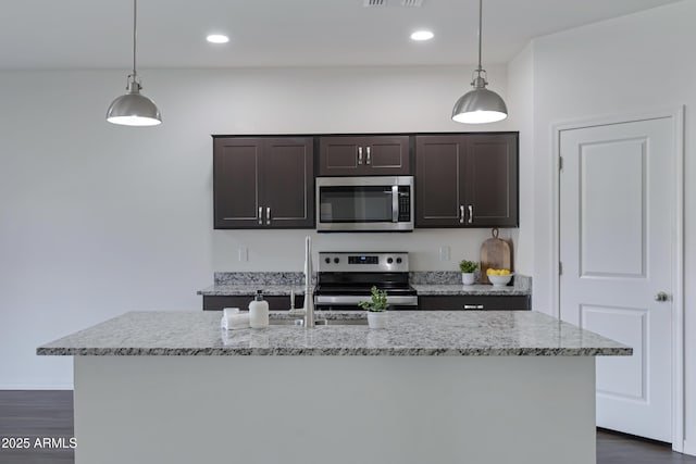 kitchen featuring appliances with stainless steel finishes, light stone countertops, a kitchen island with sink, and hanging light fixtures