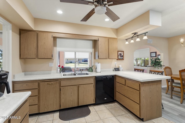 kitchen featuring a peninsula, a sink, a healthy amount of sunlight, black dishwasher, and light countertops