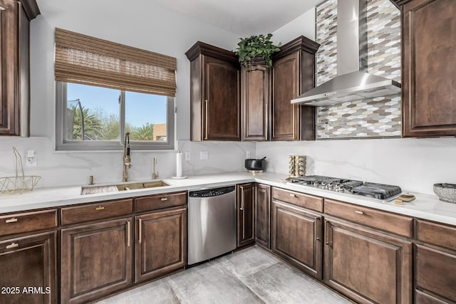 kitchen featuring appliances with stainless steel finishes, tasteful backsplash, sink, dark brown cabinets, and wall chimney exhaust hood