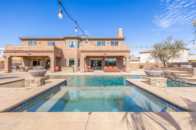 back of property featuring a pool with hot tub, a patio area, a balcony, and an outdoor fire pit