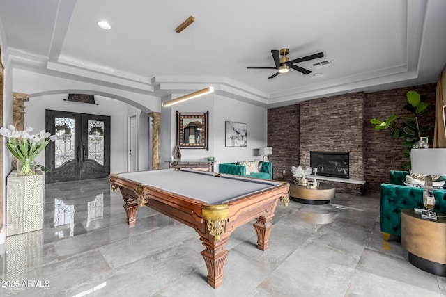 rec room with french doors, a stone fireplace, and a tray ceiling