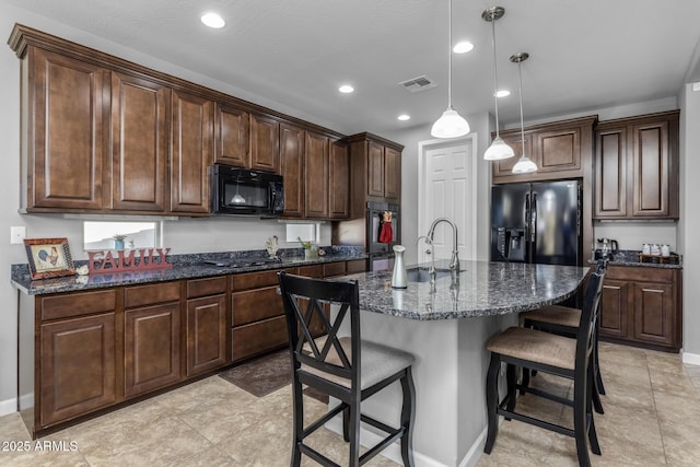 kitchen featuring an island with sink, sink, hanging light fixtures, dark brown cabinetry, and black appliances