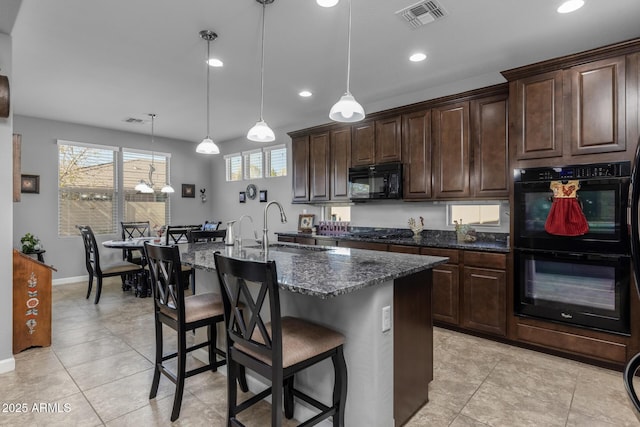 kitchen featuring sink, black appliances, hanging light fixtures, and an island with sink