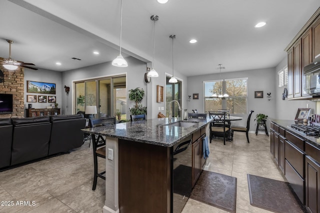 kitchen with a breakfast bar, sink, a center island with sink, pendant lighting, and black appliances