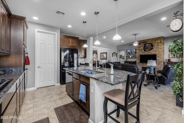 kitchen featuring a kitchen bar, sink, a center island with sink, dark stone countertops, and pendant lighting