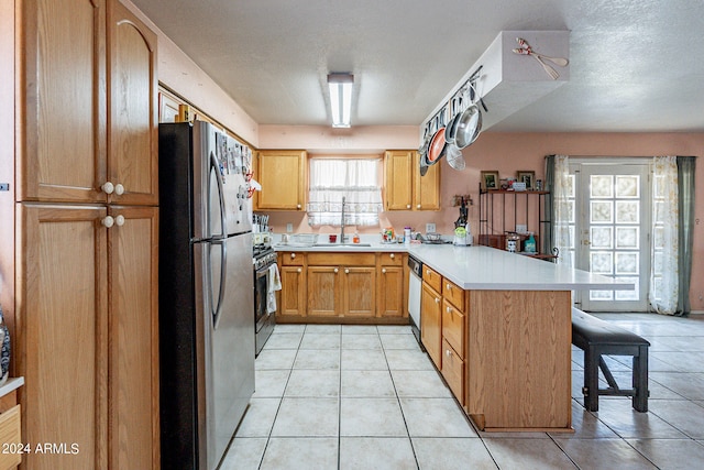 kitchen with kitchen peninsula, stainless steel appliances, sink, light tile patterned floors, and a textured ceiling