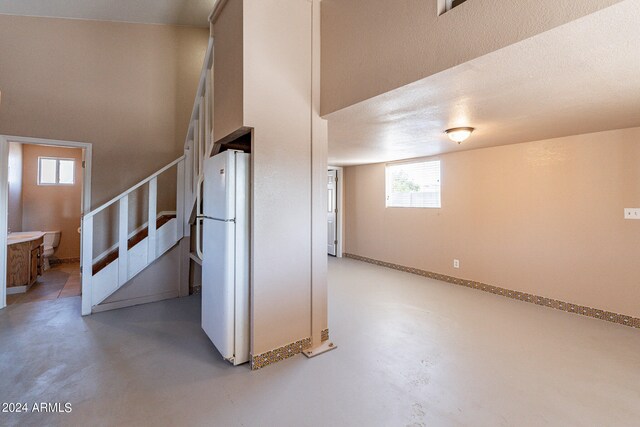 basement with a healthy amount of sunlight, a textured ceiling, and white refrigerator