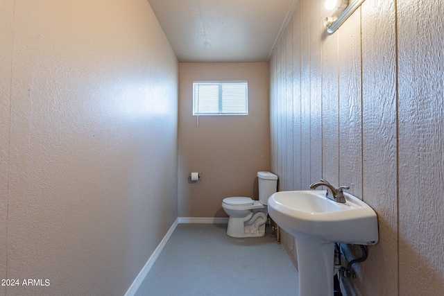 bathroom with toilet, concrete floors, and wooden walls