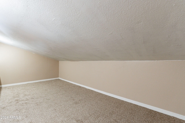 bonus room featuring a textured ceiling, vaulted ceiling, and carpet flooring