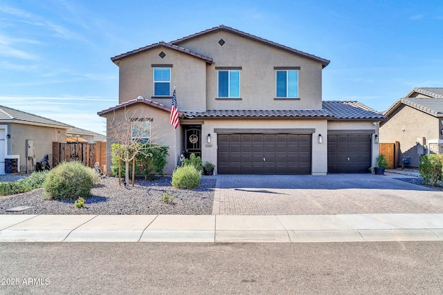 view of front of property featuring a garage, a tile roof, fence, decorative driveway, and stucco siding